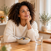 Vrouw zit bij het ontbijt aan een keukentafel.
